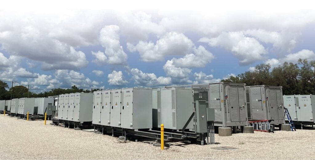 Landscape image of grey battery storage containerised units in rows with power conversion system equipment under a blue cloudy sky.